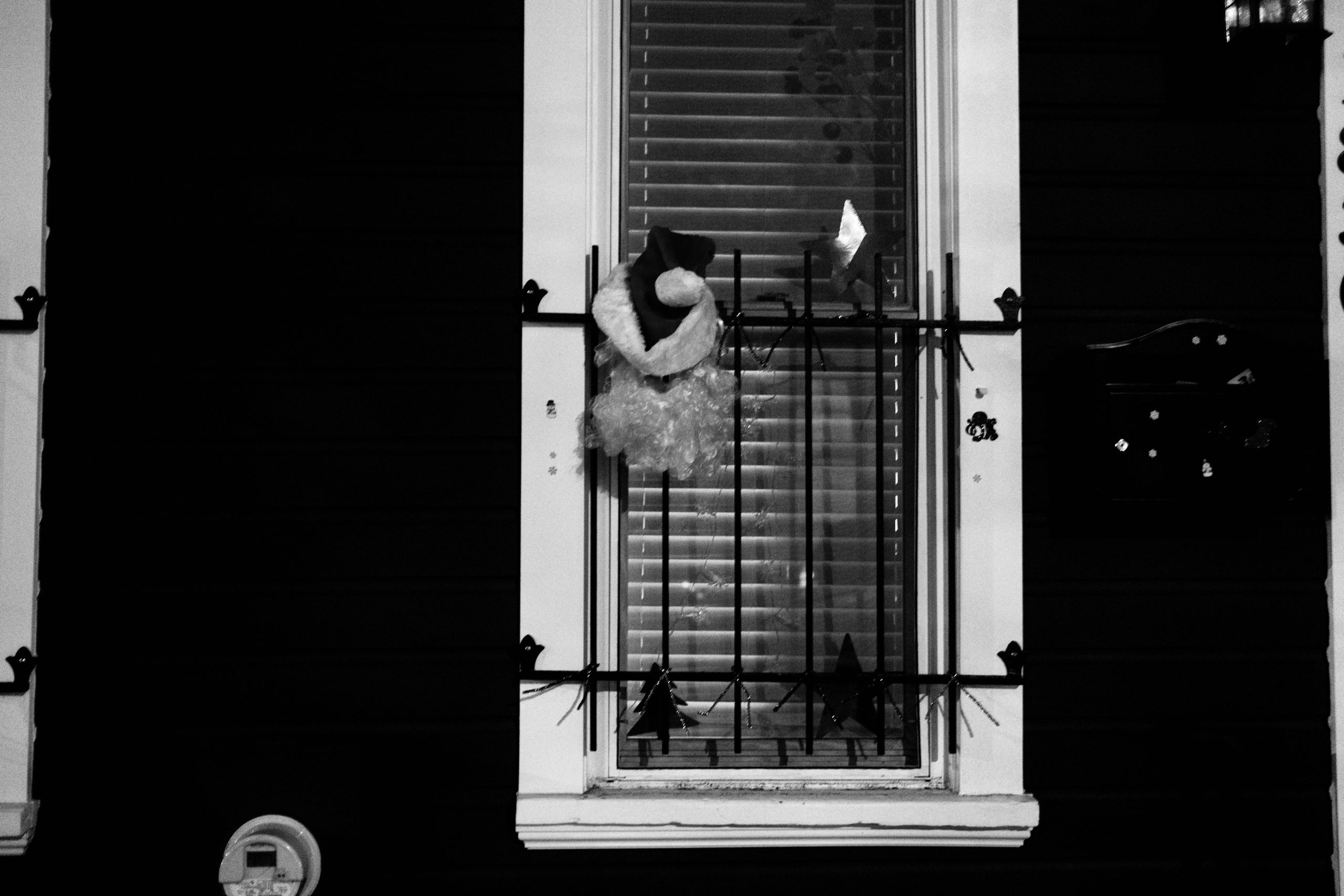 A black and white photo of a santa clause hat and beard hanging from a window with bars