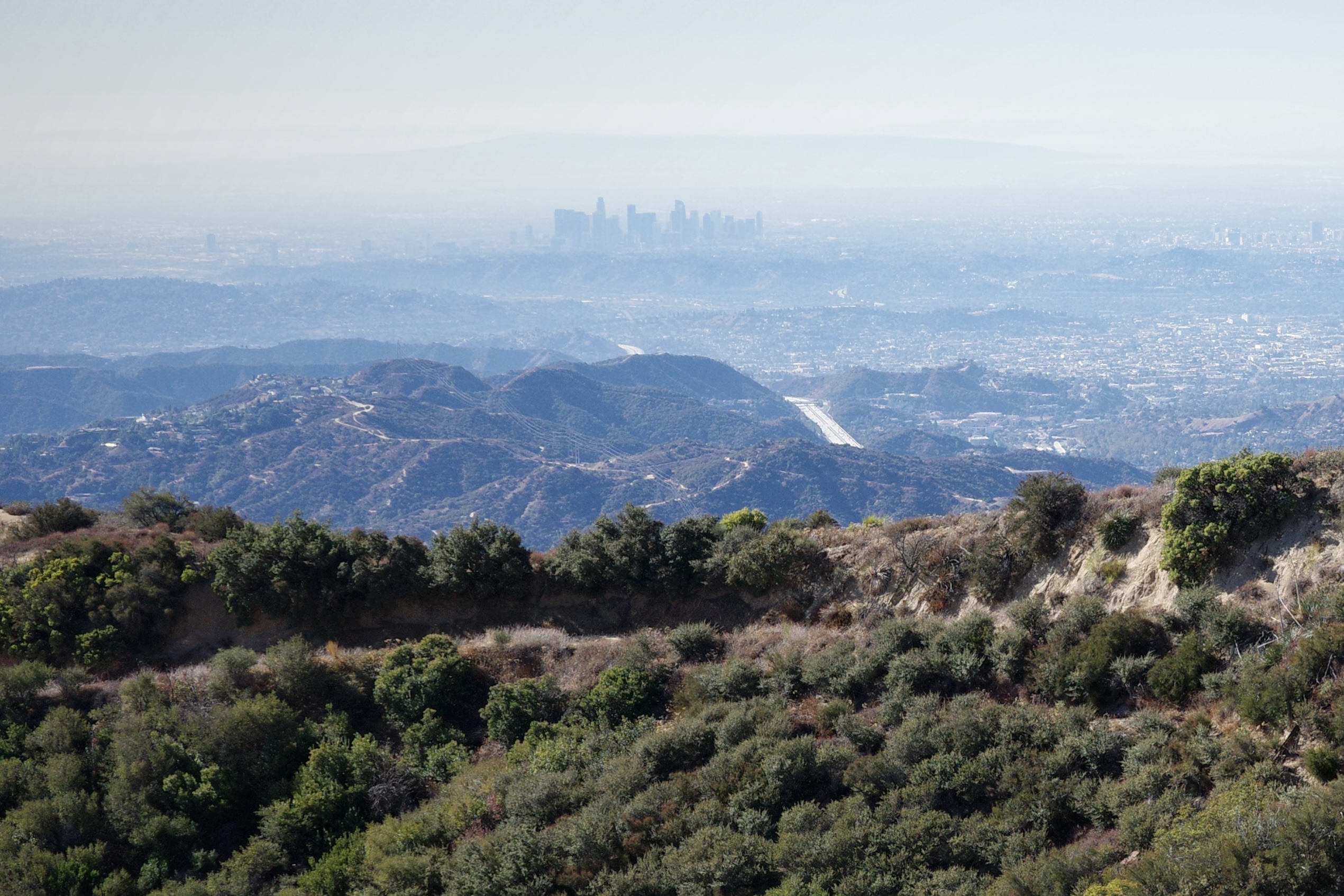 photograph of los angeles from a distance from a mountain top with a smaller mountain in the middle distance
